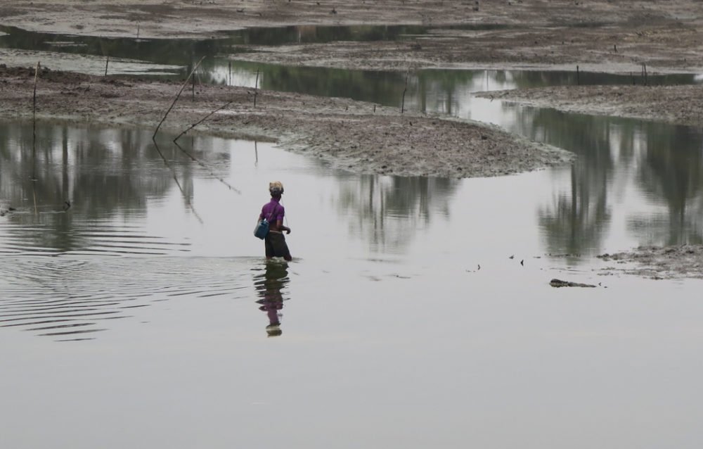 A woman wades into polluted water in search of fish (Eyre, 2017)